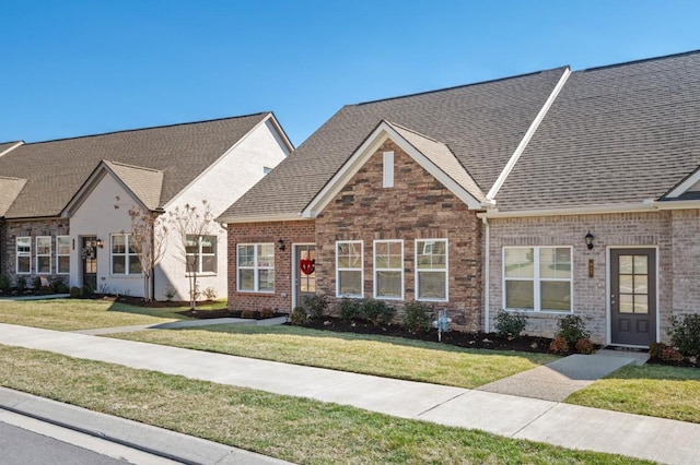 multi unit property with brick siding, a front lawn, and roof with shingles