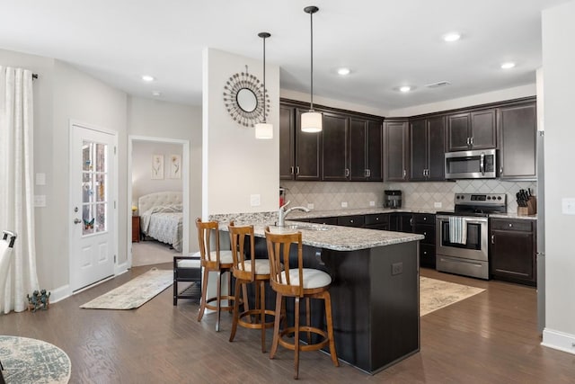 kitchen with a peninsula, dark wood-style floors, appliances with stainless steel finishes, and dark brown cabinets