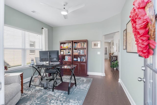 home office with a ceiling fan, visible vents, baseboards, and wood finished floors