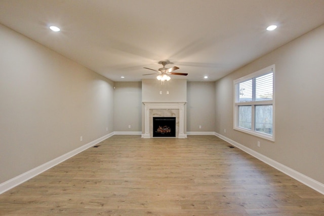 unfurnished living room featuring baseboards, ceiling fan, a premium fireplace, light wood-style floors, and recessed lighting