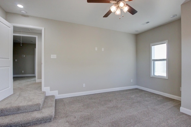 carpeted empty room featuring ceiling fan, visible vents, baseboards, and attic access