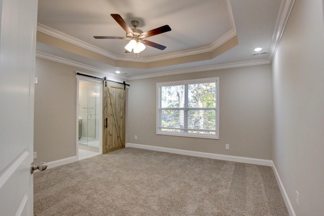 carpeted empty room with ornamental molding, a raised ceiling, baseboards, and a barn door