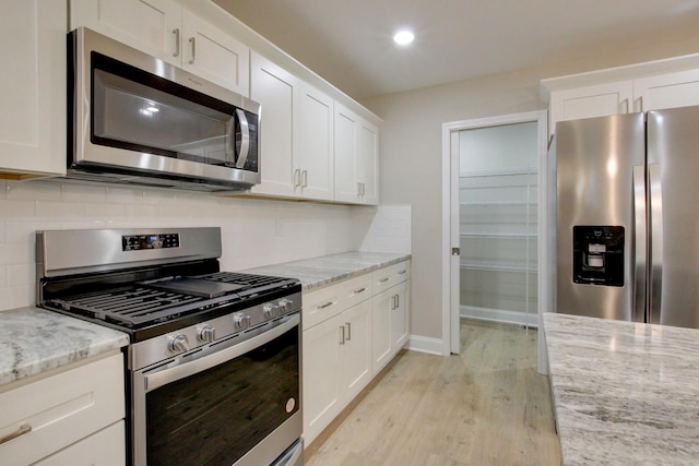 kitchen featuring stainless steel appliances, white cabinets, decorative backsplash, and light wood finished floors