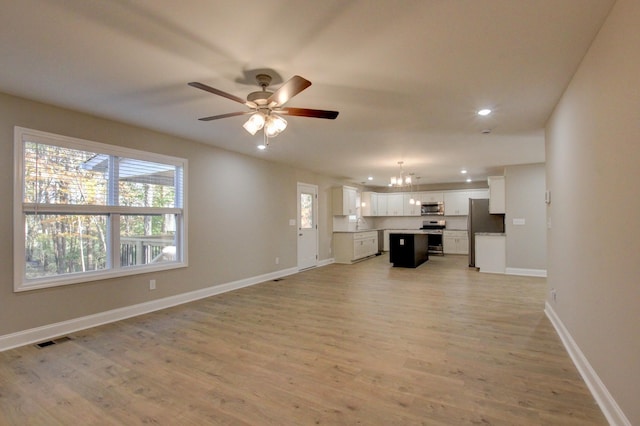 unfurnished living room featuring recessed lighting, ceiling fan with notable chandelier, visible vents, baseboards, and light wood-type flooring