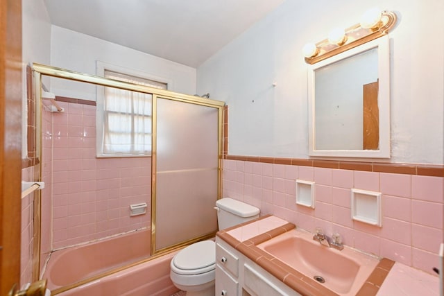 bathroom featuring tile walls, toilet, wainscoting, combined bath / shower with glass door, and vanity