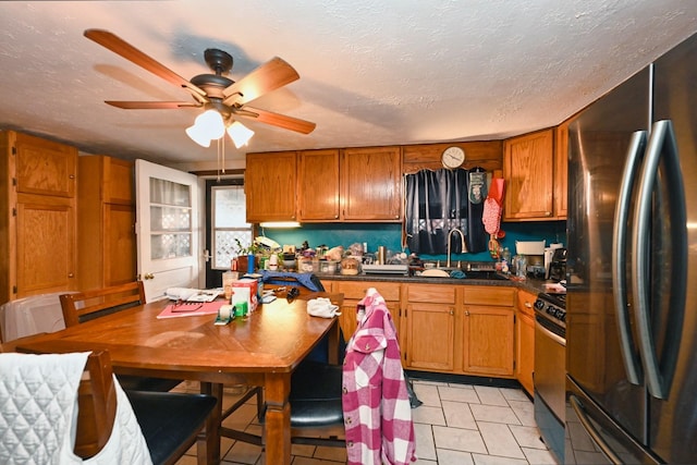 kitchen featuring stove, a sink, freestanding refrigerator, brown cabinetry, and dark countertops