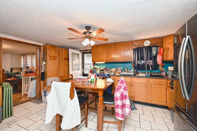 kitchen with brown cabinets, dark countertops, freestanding refrigerator, a sink, and a textured ceiling