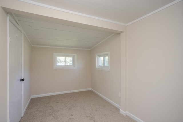 spare room with vaulted ceiling, light colored carpet, crown molding, and baseboards