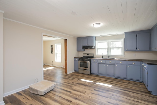 kitchen with dark countertops, gas range, wood finished floors, under cabinet range hood, and baseboards