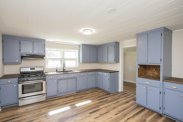 kitchen featuring dark countertops, gas range, under cabinet range hood, and a sink