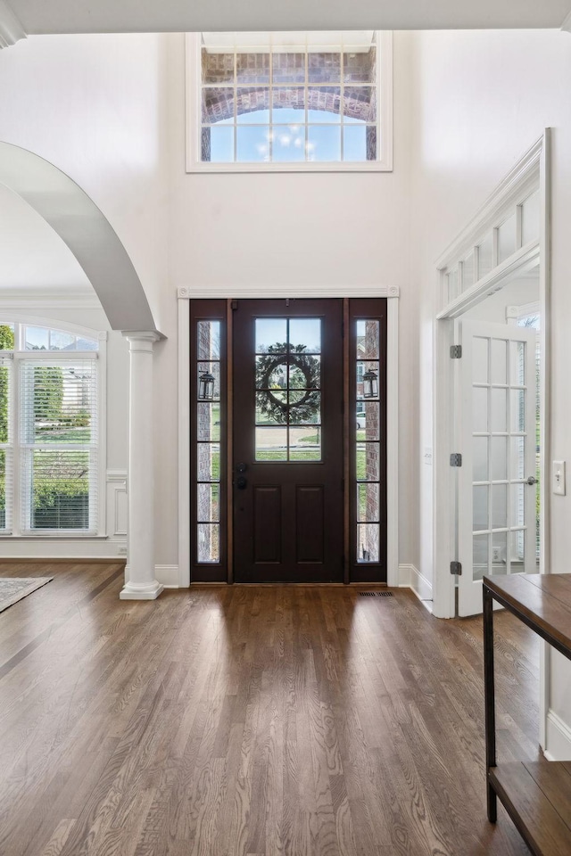 foyer entrance featuring arched walkways, a towering ceiling, ornate columns, and wood finished floors