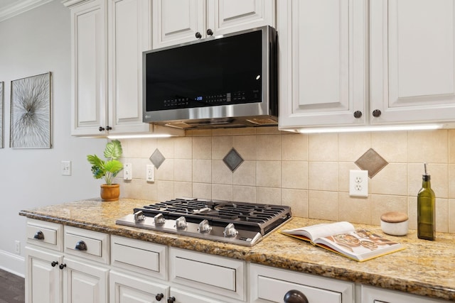 kitchen featuring stainless steel appliances, light stone counters, decorative backsplash, and white cabinets