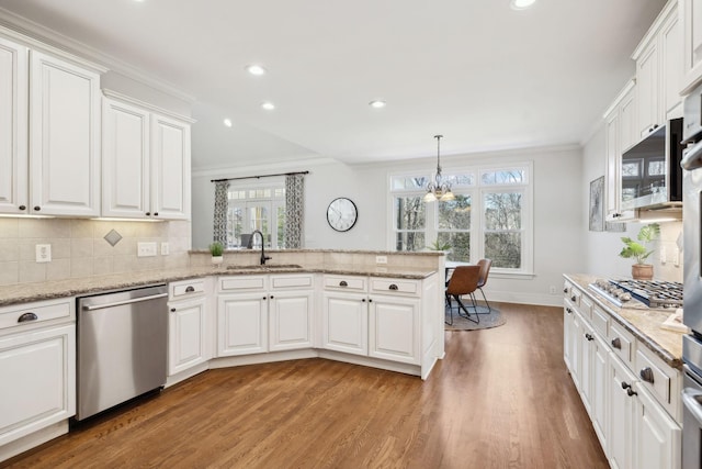 kitchen with appliances with stainless steel finishes, ornamental molding, white cabinets, a sink, and a peninsula