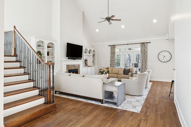 living room featuring stairway, ornamental molding, wood finished floors, a lit fireplace, and baseboards