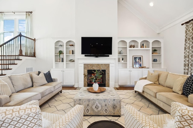 living room featuring visible vents, built in features, ornamental molding, a lit fireplace, and high vaulted ceiling