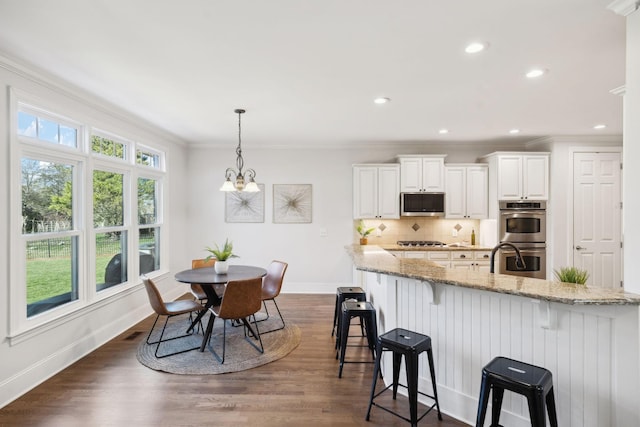 kitchen featuring a breakfast bar, dark wood-style flooring, appliances with stainless steel finishes, decorative backsplash, and light stone countertops