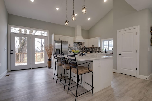 kitchen featuring stainless steel fridge, white cabinets, a breakfast bar area, custom exhaust hood, and light wood-style floors