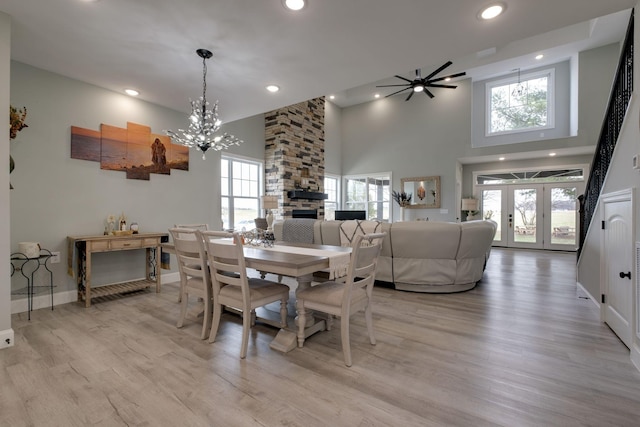 dining room featuring a fireplace, light wood finished floors, recessed lighting, a high ceiling, and ceiling fan with notable chandelier