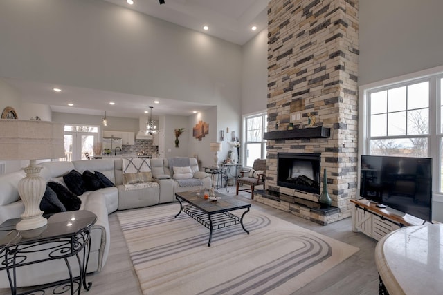 living area with a stone fireplace, light wood finished floors, a towering ceiling, and recessed lighting