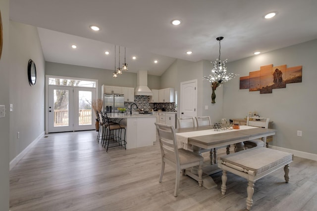 dining room featuring a chandelier, light wood-type flooring, vaulted ceiling, and baseboards