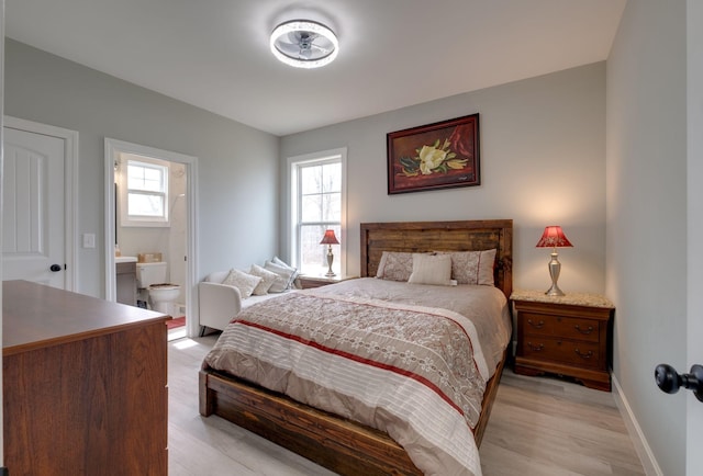 bedroom with multiple windows, ensuite bath, light wood-style flooring, and baseboards