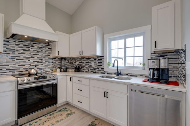 kitchen featuring custom range hood, stainless steel appliances, light countertops, white cabinetry, and a sink