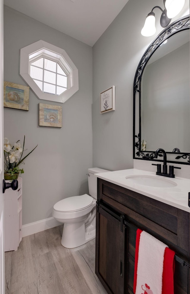 half bath featuring vanity, wood finished floors, toilet, and baseboards