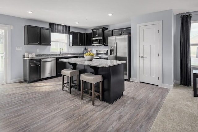 kitchen with a kitchen island, a kitchen breakfast bar, appliances with stainless steel finishes, dark cabinetry, and light stone countertops