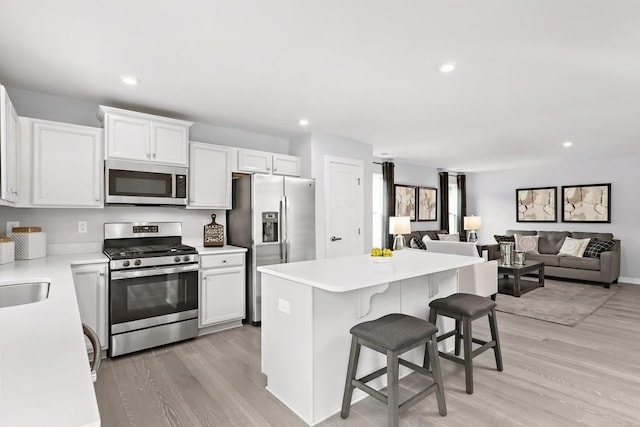 kitchen with stainless steel appliances, white cabinetry, light wood-style flooring, and a kitchen breakfast bar