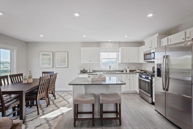 kitchen with a kitchen island, a breakfast bar area, stainless steel appliances, white cabinetry, and a sink