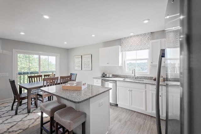 kitchen featuring appliances with stainless steel finishes, a sink, a kitchen island, light stone countertops, and a kitchen bar