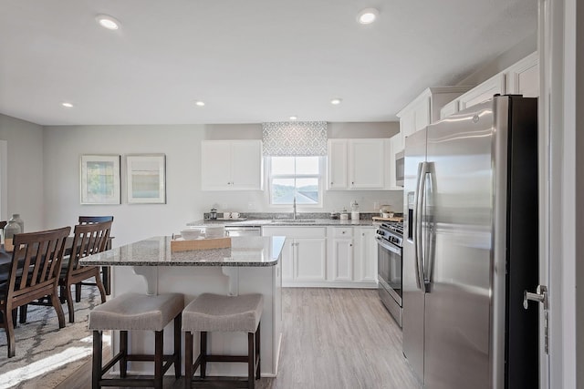 kitchen featuring light stone counters, a breakfast bar area, stainless steel appliances, a sink, and a kitchen island