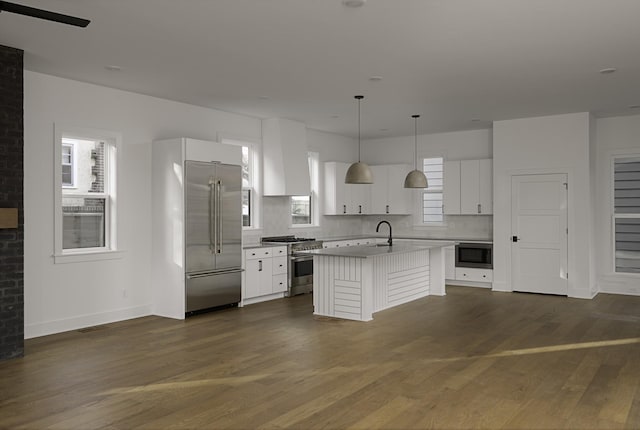 kitchen featuring built in appliances, dark wood-style flooring, a sink, wall chimney range hood, and an island with sink