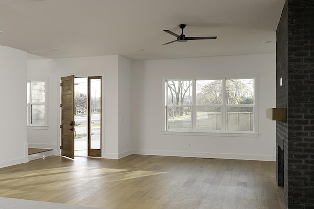 unfurnished living room with ceiling fan, a brick fireplace, wood finished floors, and baseboards