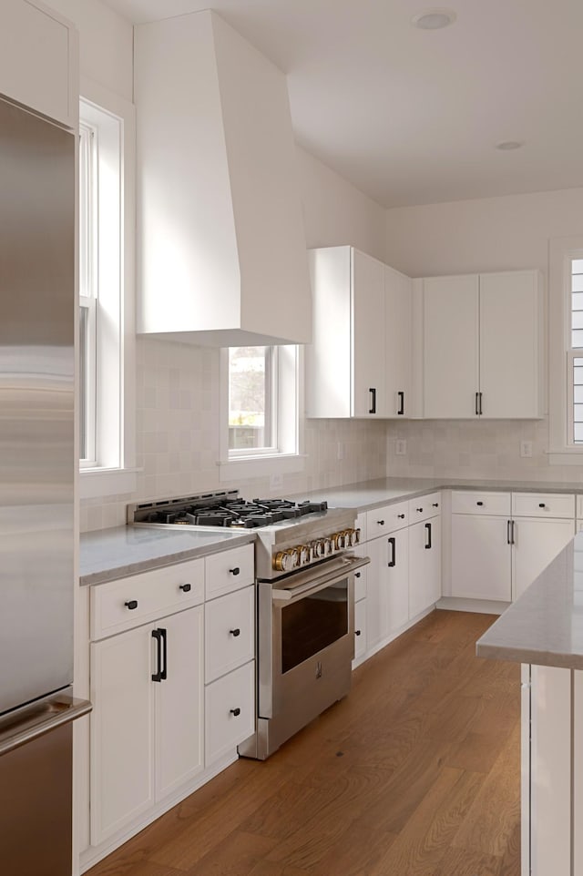 kitchen with light wood-type flooring, a healthy amount of sunlight, wall chimney exhaust hood, and high end appliances