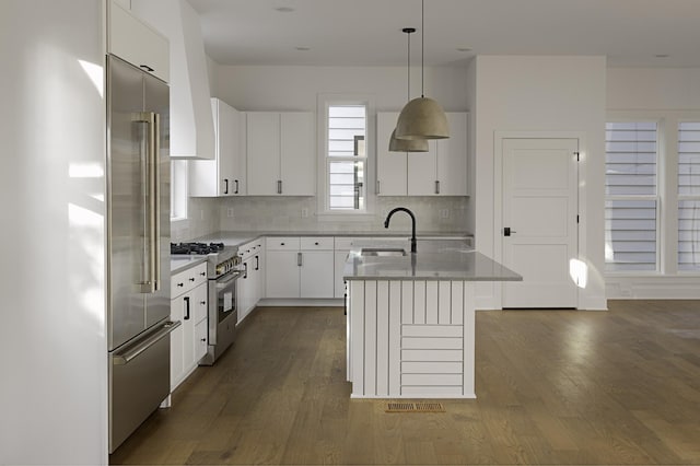 kitchen with decorative light fixtures, dark wood finished floors, tasteful backsplash, a sink, and high quality appliances