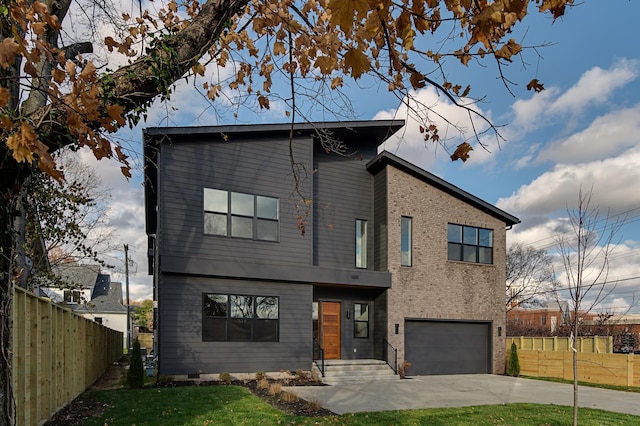 contemporary home featuring a garage, concrete driveway, brick siding, and fence