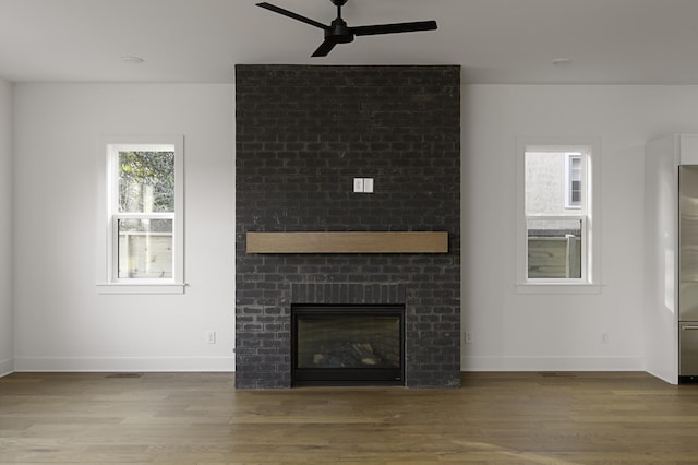 unfurnished living room with a ceiling fan, a brick fireplace, baseboards, and wood finished floors