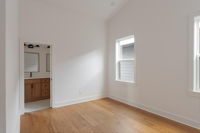 spare room featuring light wood-type flooring, lofted ceiling, and baseboards