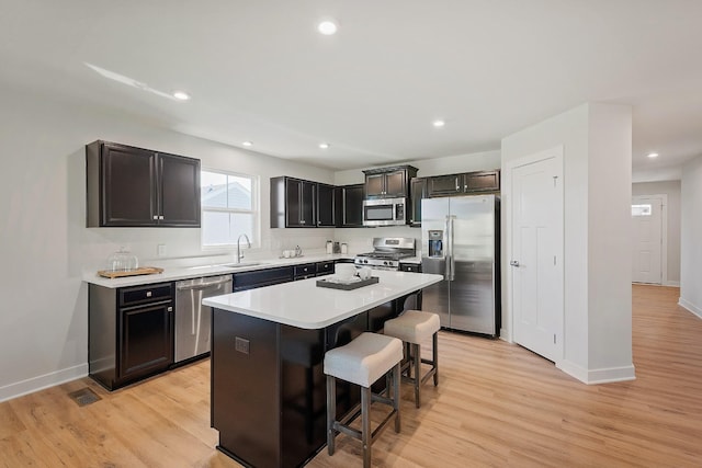 kitchen featuring stainless steel appliances, light wood-style floors, a sink, and a kitchen breakfast bar