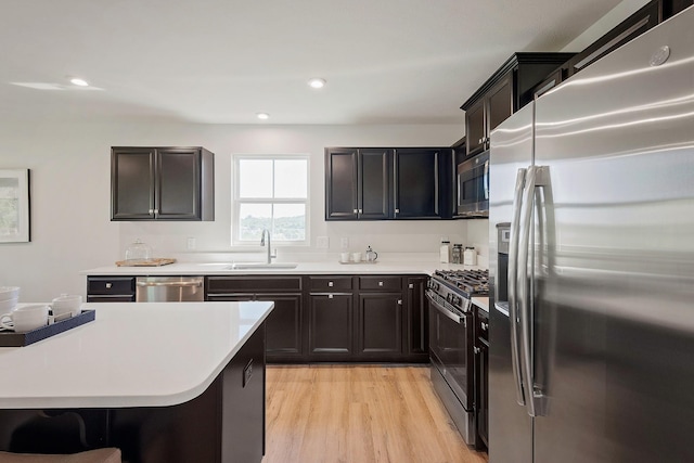 kitchen with appliances with stainless steel finishes, light countertops, a sink, and light wood finished floors