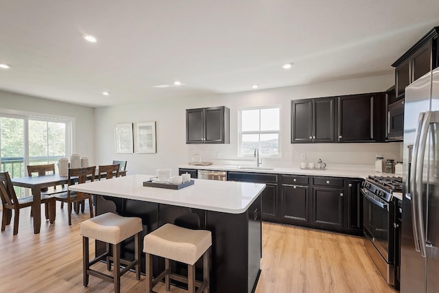 kitchen with a kitchen island, a sink, appliances with stainless steel finishes, a wealth of natural light, and a kitchen bar