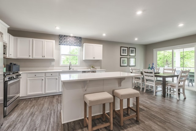 kitchen featuring gas range, a breakfast bar, dark wood-type flooring, light countertops, and a sink