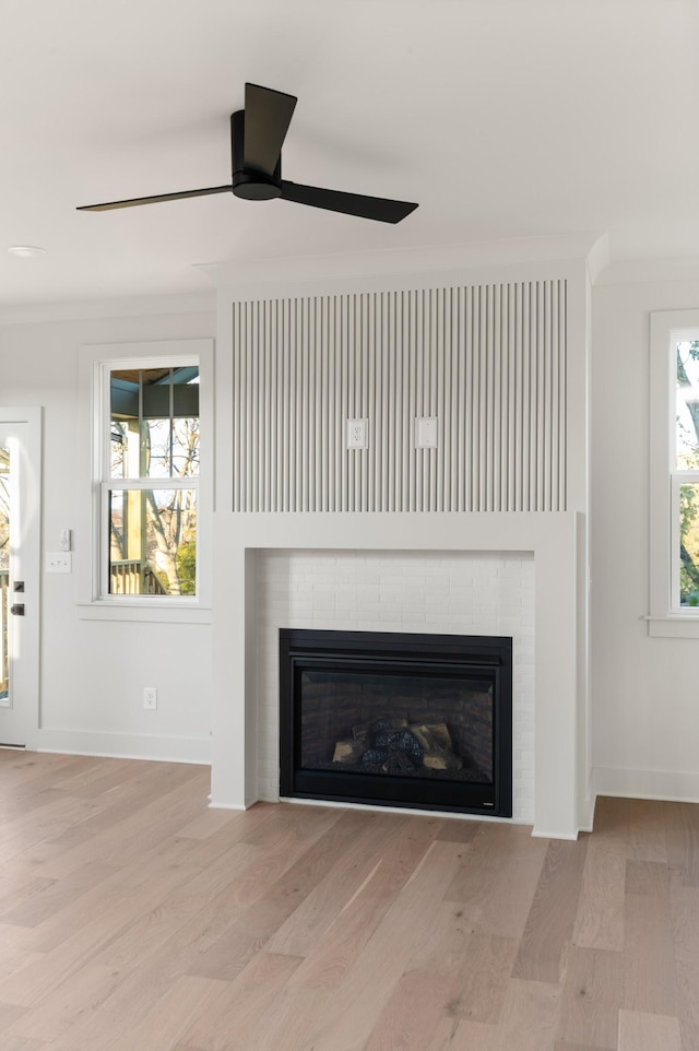 interior details featuring wood finished floors, a glass covered fireplace, a ceiling fan, and baseboards