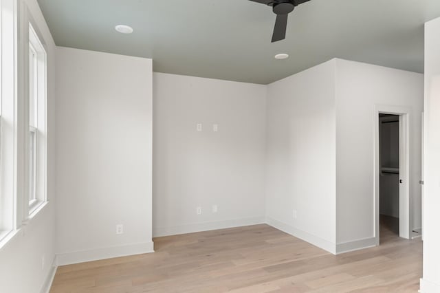 spare room featuring light wood finished floors, a ceiling fan, and baseboards