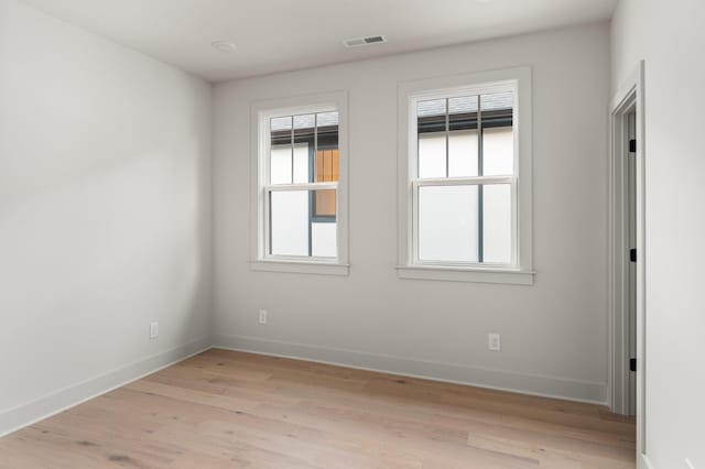 spare room with baseboards, light wood-style flooring, visible vents, and a wealth of natural light