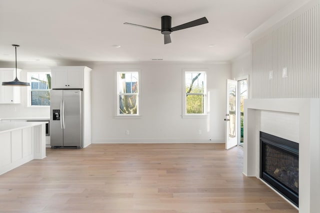 unfurnished living room with a ceiling fan, a glass covered fireplace, baseboards, and light wood finished floors