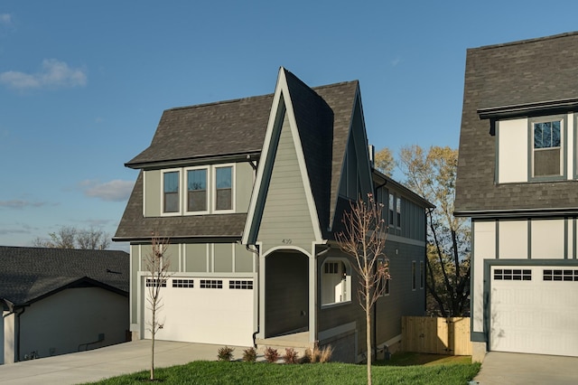 tudor-style house with concrete driveway, board and batten siding, an attached garage, and roof with shingles