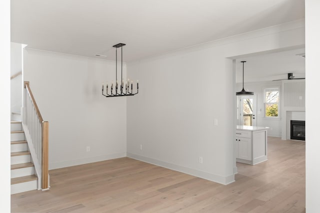 unfurnished dining area with baseboards, a glass covered fireplace, light wood-style flooring, stairway, and ornamental molding