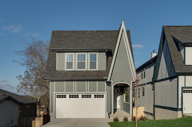 tudor-style house featuring driveway, a garage, board and batten siding, and roof with shingles